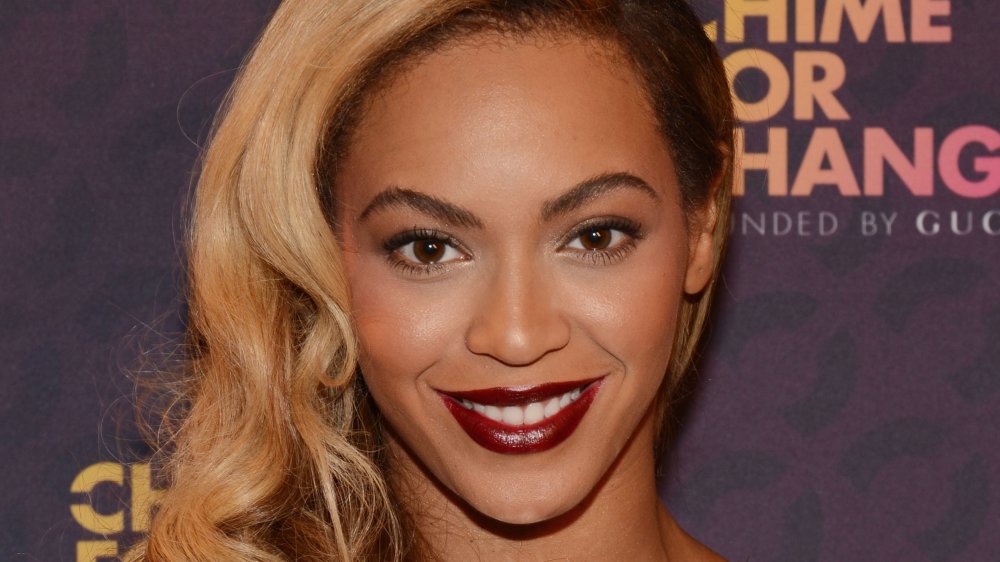 Beyoncé con el pelo largo rubio y lápiz labial rojo oscuro, sonriendo