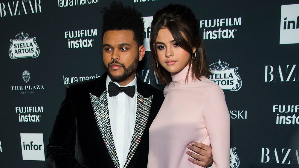 El Weeknd en traje de terciopelo negro y pajarita, Selena Gomez con un vestido rosa, posando juntos en la alfombra roja