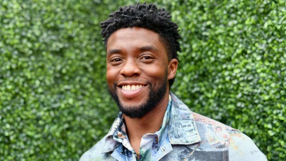 Chadwick Boseman con una chaqueta de jean multicolor y abotonado, sonriendo afuera