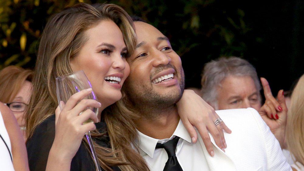 Chrissy Teigen sosteniendo una copa de champán, abrazando a John Legend