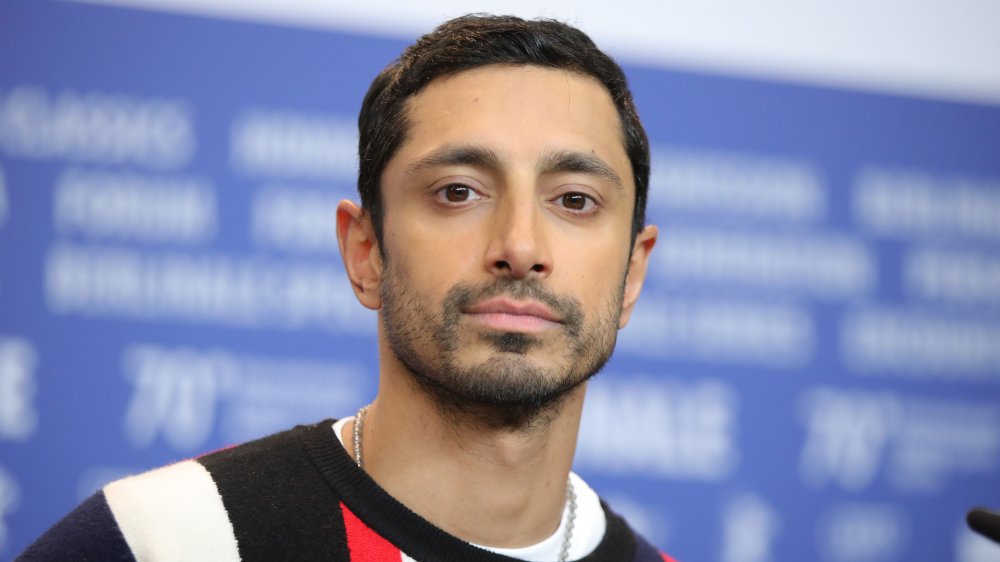 Riz Ahmed en un suéter negro, rojo y blanco, posando durante una entrevista con una expresión neutra