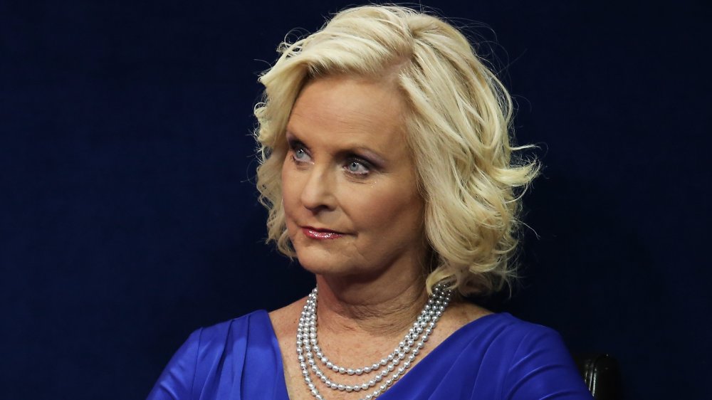 Cindy McCain con un vestido azul y perlas, mirando hacia un lado con una expresión neutra