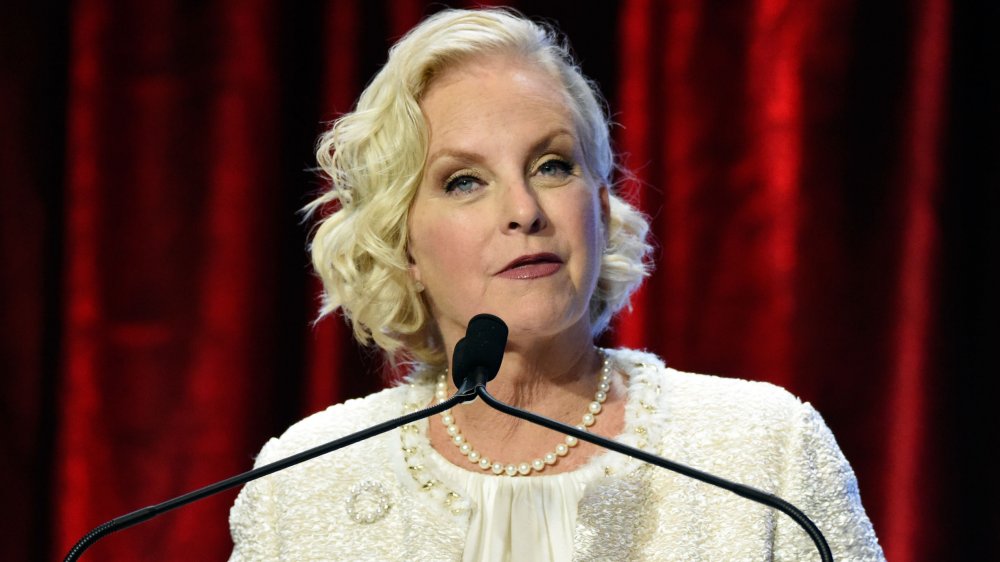 Cindy McCain con un vestido blanco y perlas, hablando en un evento