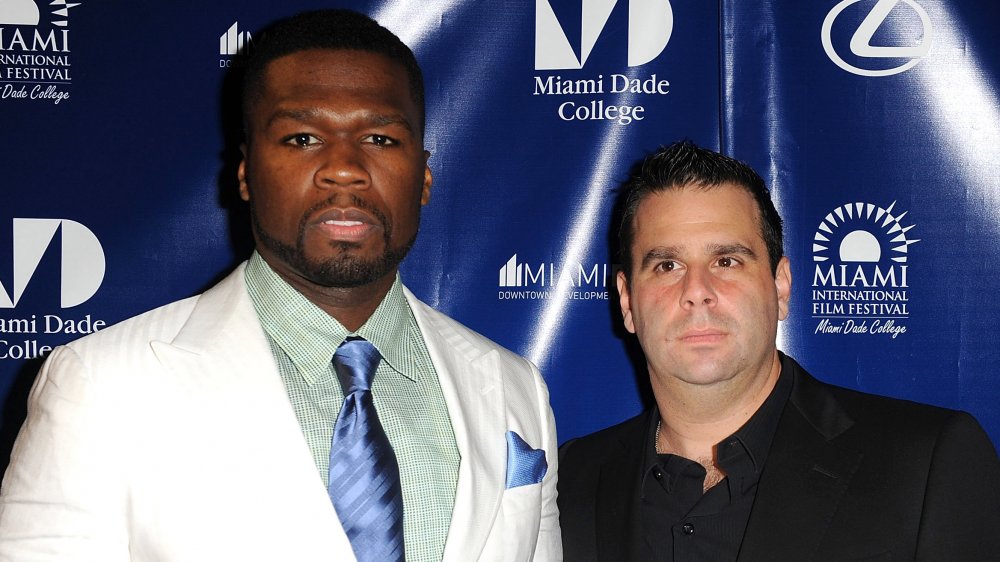 50 Cent en traje blanco y corbata azul, Randall Emmett con traje negro