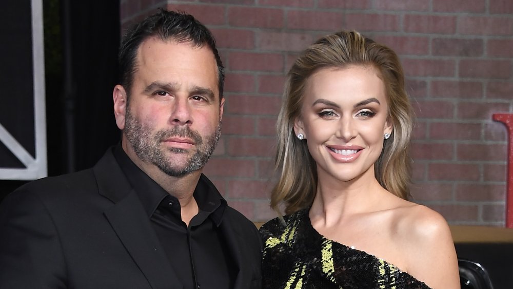 Randall Emmett en traje negro, Lala Kent sonriendo en un vestido negro y amarillo