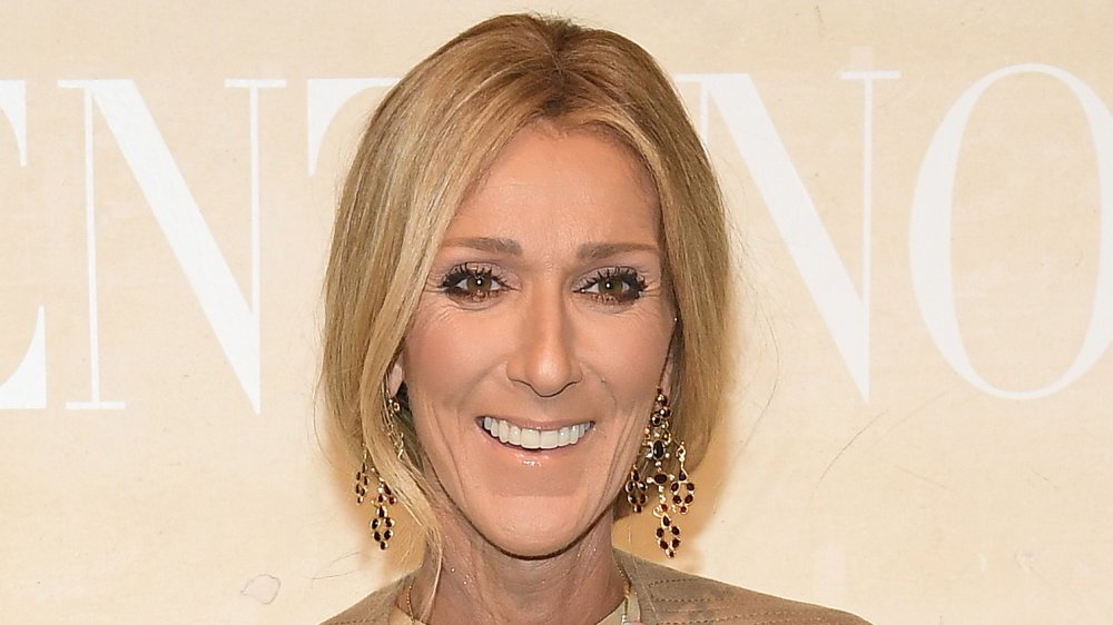 Céline Dion con un traje beige y pendientes colgantes, sonriendo grande