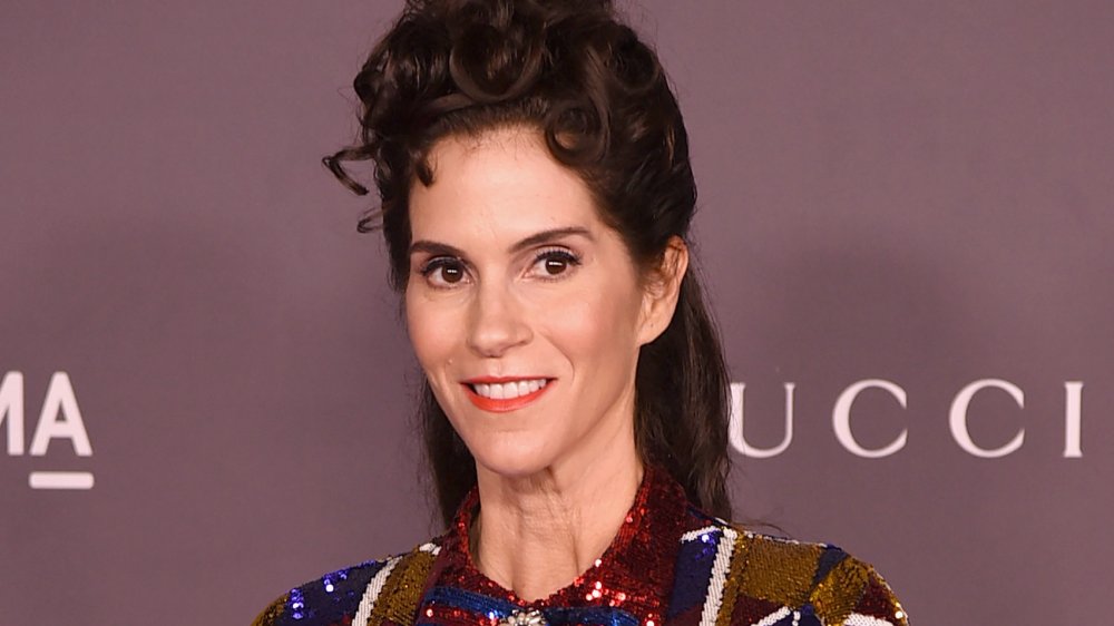 Jami Gertz en un vestido rojo, azul y dorado brillante, sonriendo y mirando hacia un lado