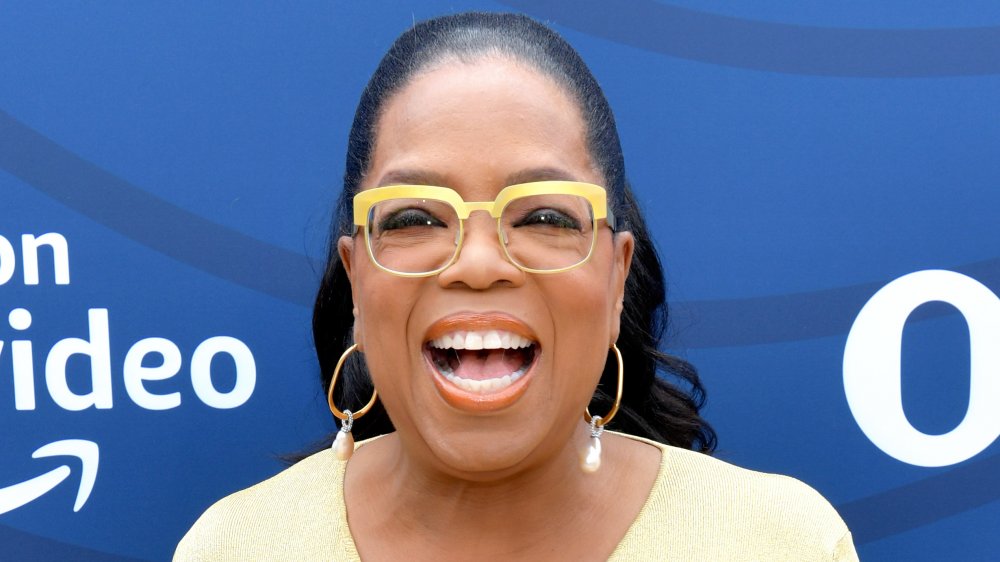 Oprah Winfrey con un vestido y gafas amarillas, riendo mientras mira directamente a la cámara