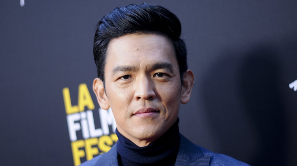 John Cho en un blazer azul y cuello de tortuga, posando con una expresión seria