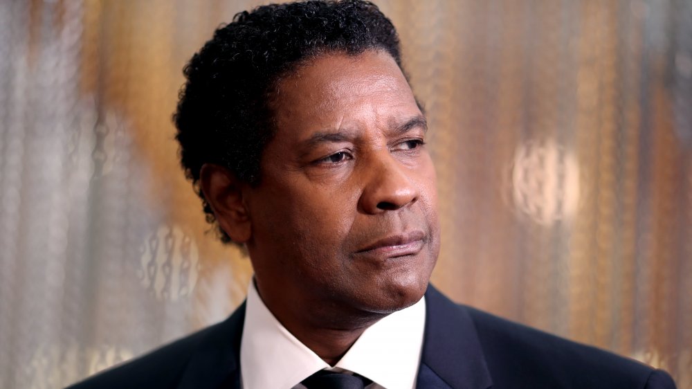 Denzel Washington en un clásico traje negro y combo de corbata, que se ve serio mientras mira hacia un lado