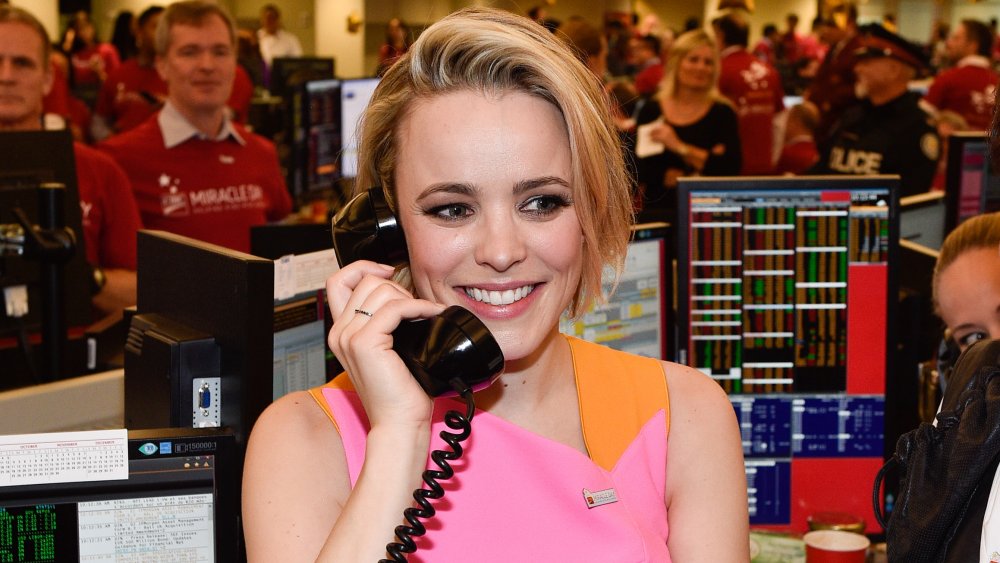 Rachel McAdams con un vestido naranja y rosa, sonriendo mientras habla por teléfono