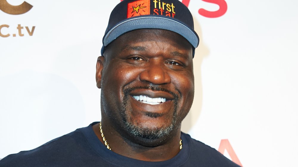 Shaquille O'Neal sonriendo con una camiseta azul y sombrero