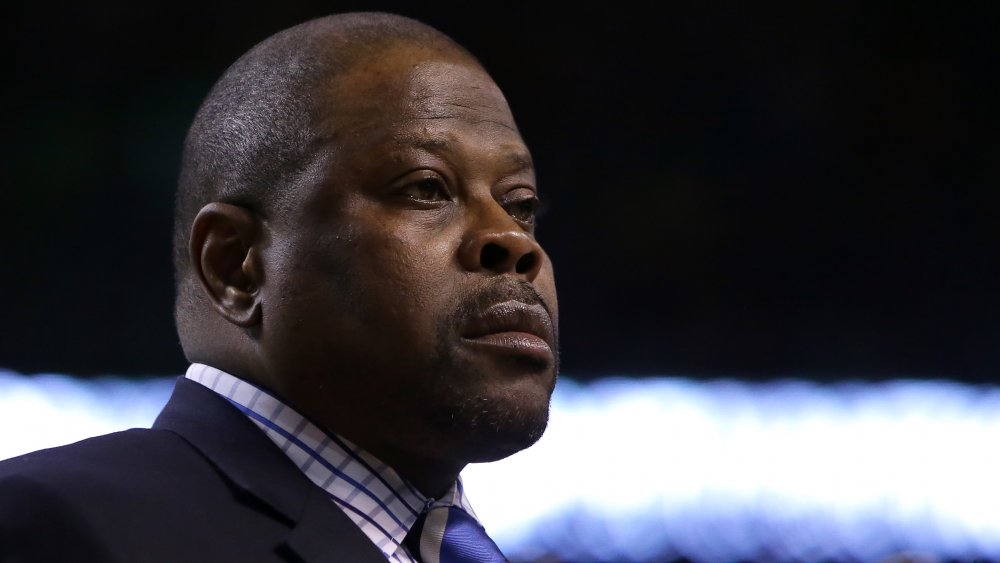 Patrick Ewing con un blazer azul y camisa a cuadros, mirando hacia un lado con una expresión seria