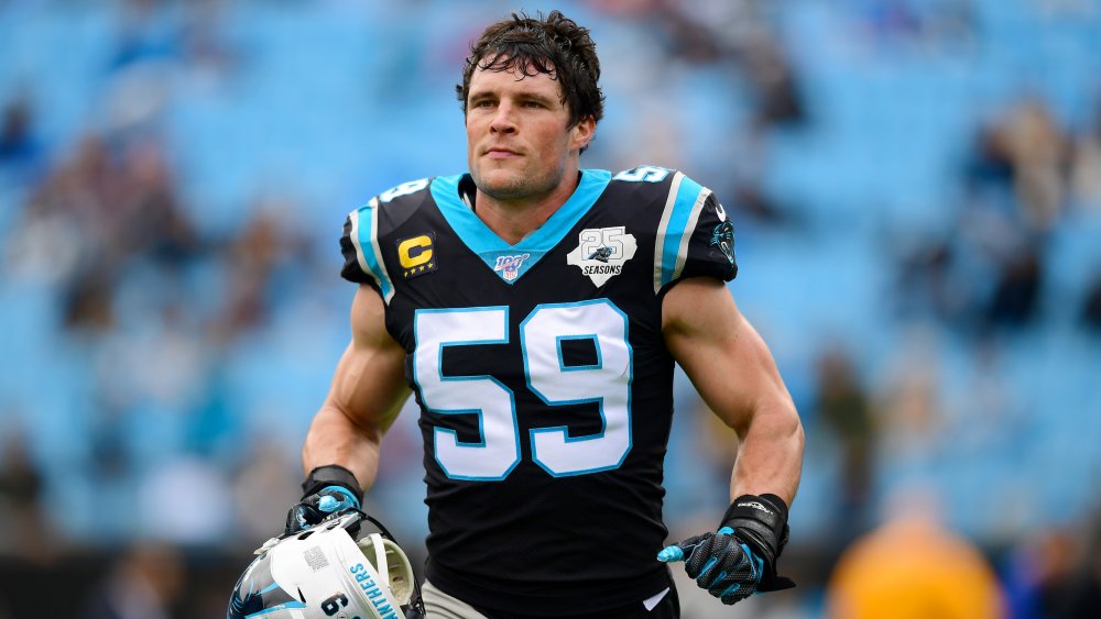 Luke Kuechly corriendo hacia el campo, sosteniendo su casco