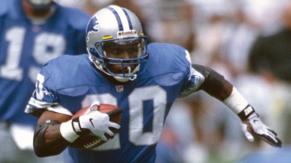 Barry Sanders corriendo por el campo, agarrando un balón de fútbol