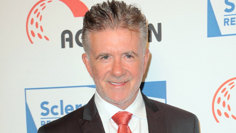 Alan Thicke sonriendo en traje y corbata roja