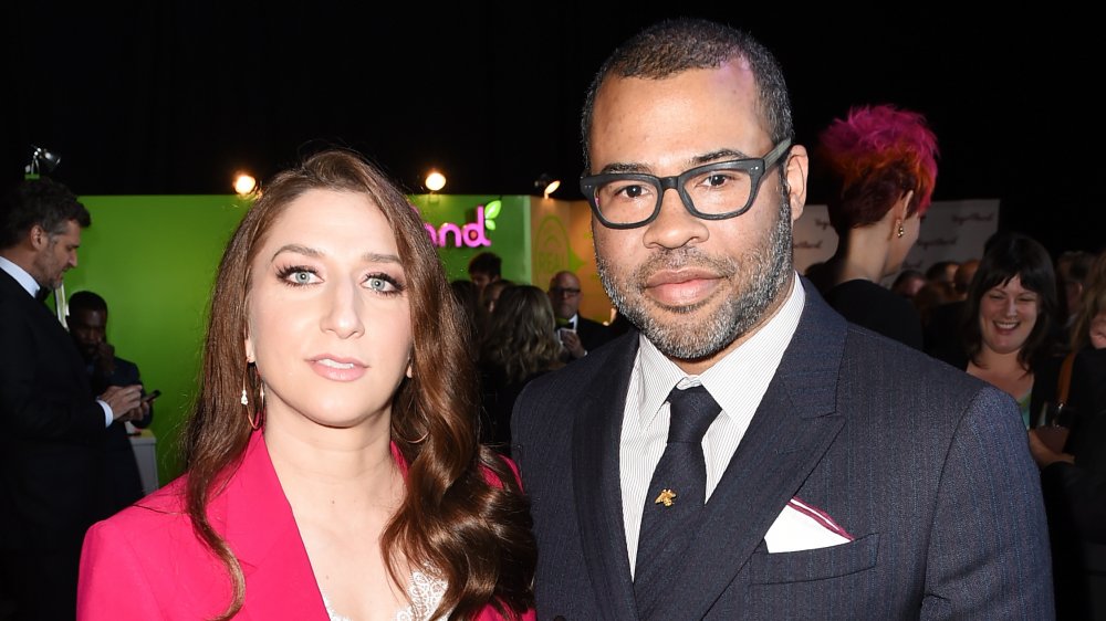 Chelsea Peretti en un blazer rosa, Jordan Peele con un traje y gafas de rayas de alfiler negro y azul