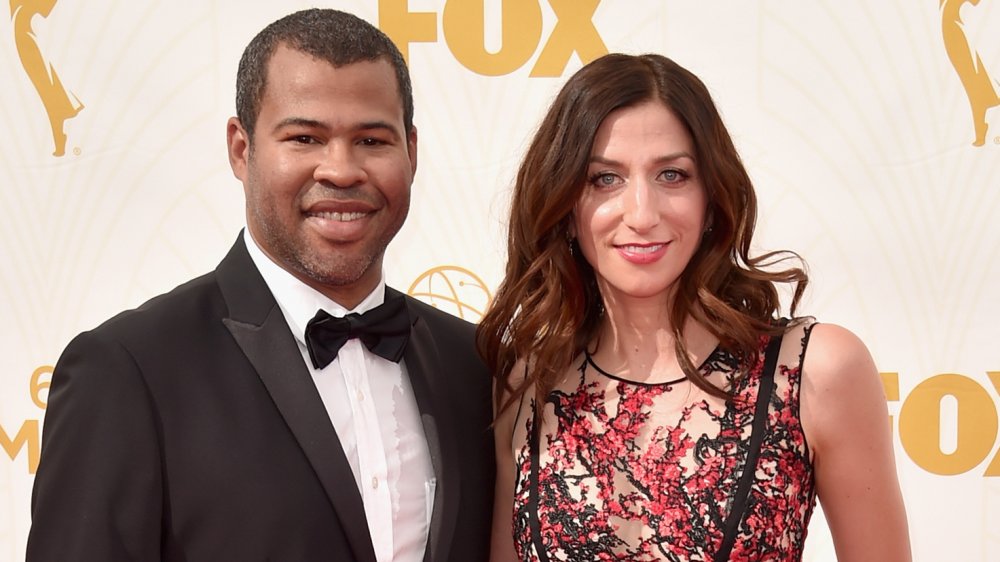 Jordan Peele con traje negro, Chelsea Peretti con un vestido negro y rojo