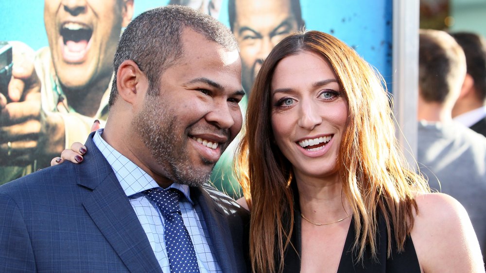 Jordan Peele en un traje azul, Chelsea Peretti con un vestido negro, ambos sonriendo grande