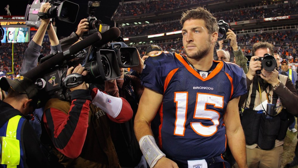 Tim Tebow con un uniforme de Denver Broncos, rodeado de reporteros