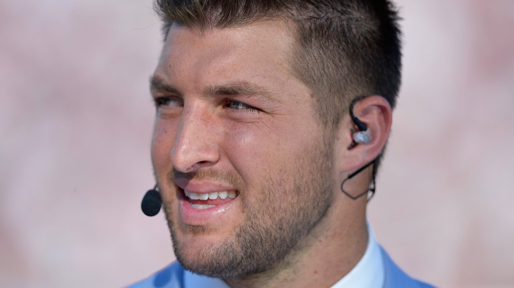 Tim Tebow hablando en un micrófono, mirando hacia un lado