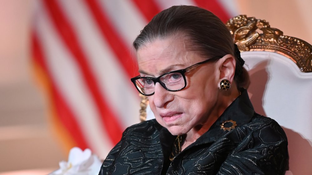 Ruth Bader Ginsburg sentado, pendientes de oro y gafas negras