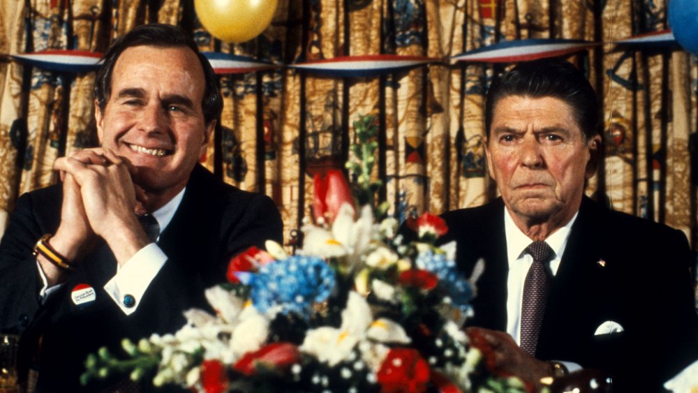 George H.W. Bush y Ronald Reagan sentados con flores frente a ellos