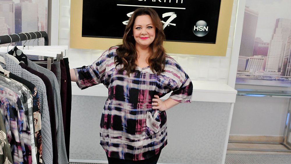 Melissa McCarthy posando junto a un perchero para su línea de ropa Seven7