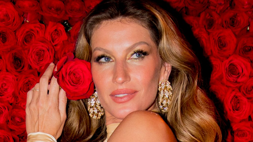 Gisele B-ndchen sosteniendo una rosa frente a un muro de rosas