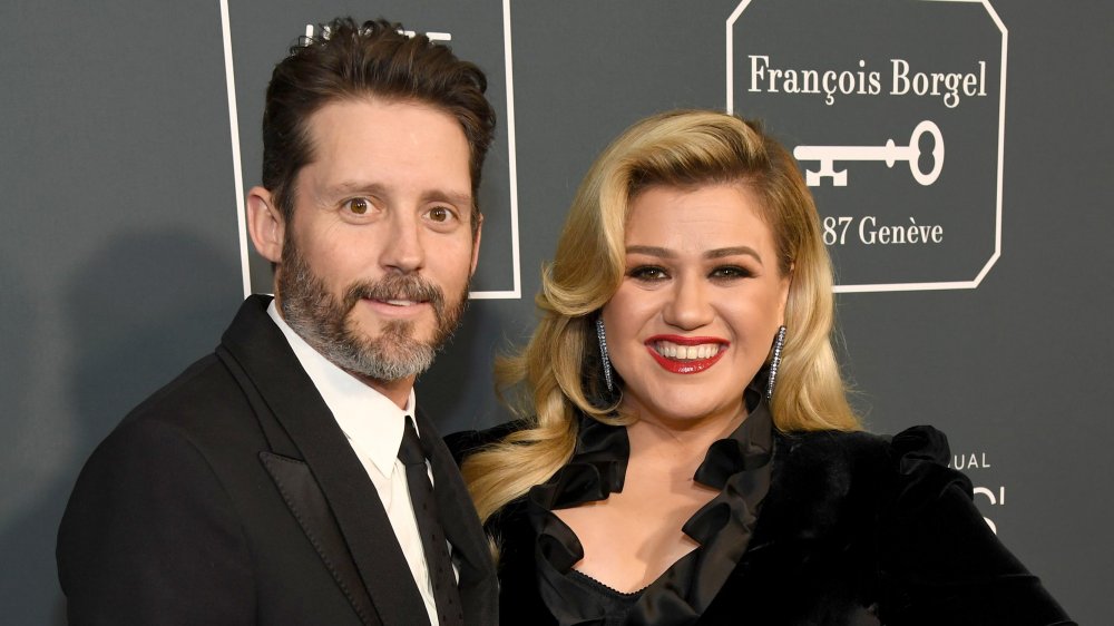 Brandon Blackstock y Kelly Clarkson, ambos sonriendo mientras posan brazo en brazo en la alfombra roja