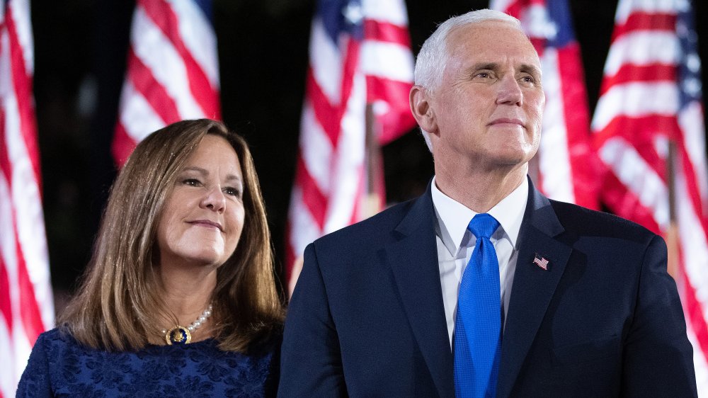 Karen y Mike Pence miran y sonríen frente a las banderas de EE.UU.