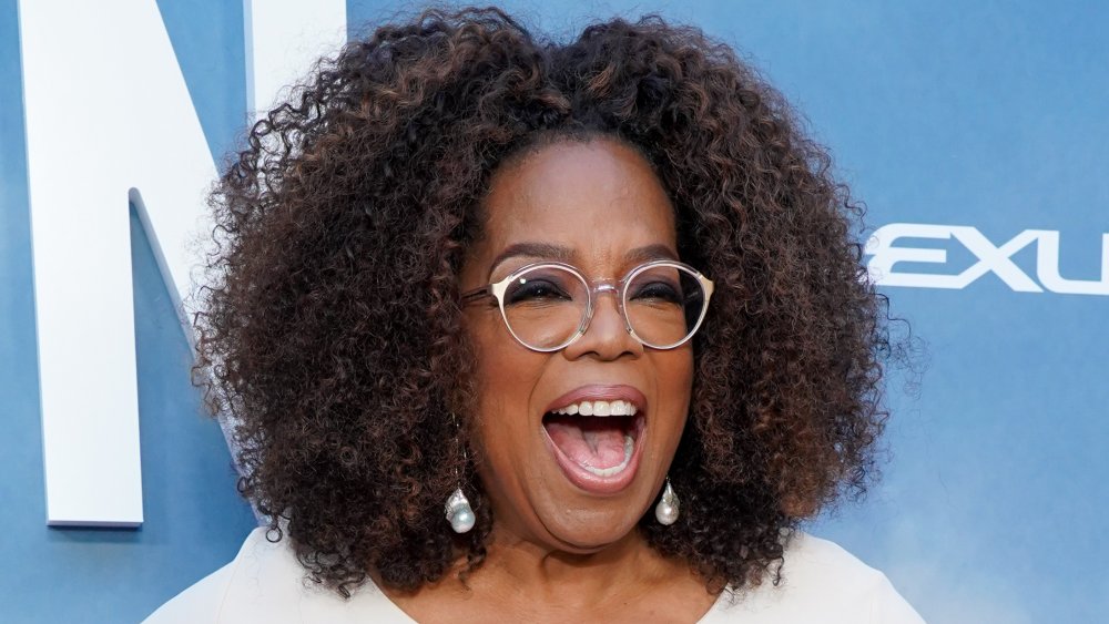 Oprah Winfrey con un traje blanco, riendo en la alfombra roja