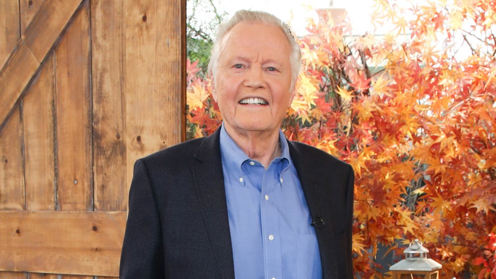 Jon Voight sonriendo frente a las hojas de otoño