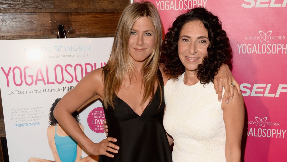 Jennifer Aniston y la inventora de Yogalosophy Mandy Ingber, sonriendo y posando del brazo