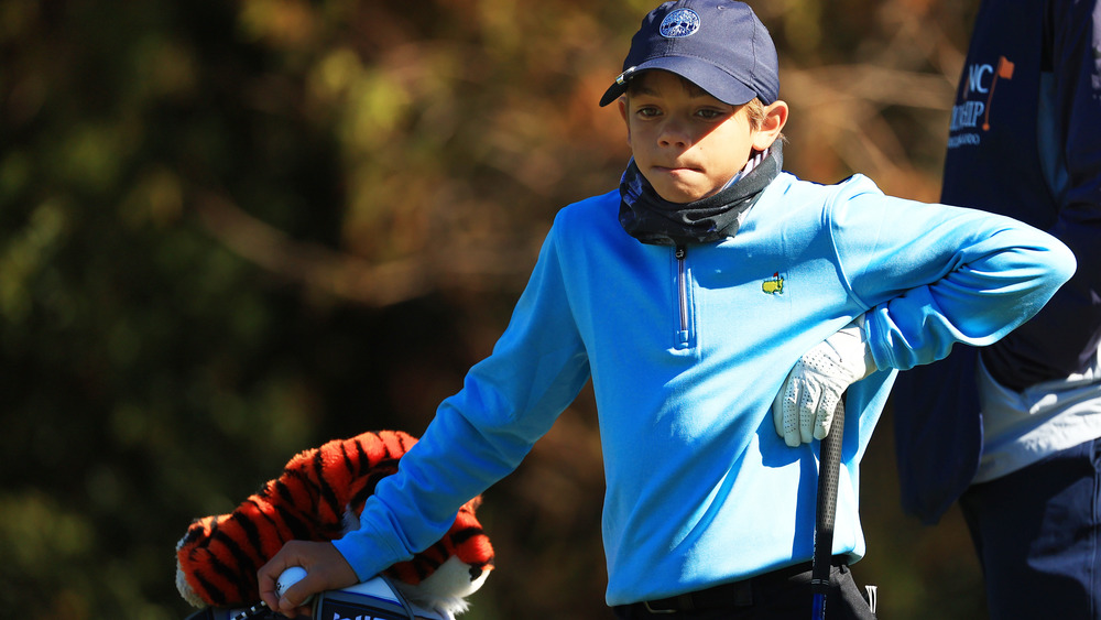 Charlie Woods apoyado en un palo de golf y una bolsa 