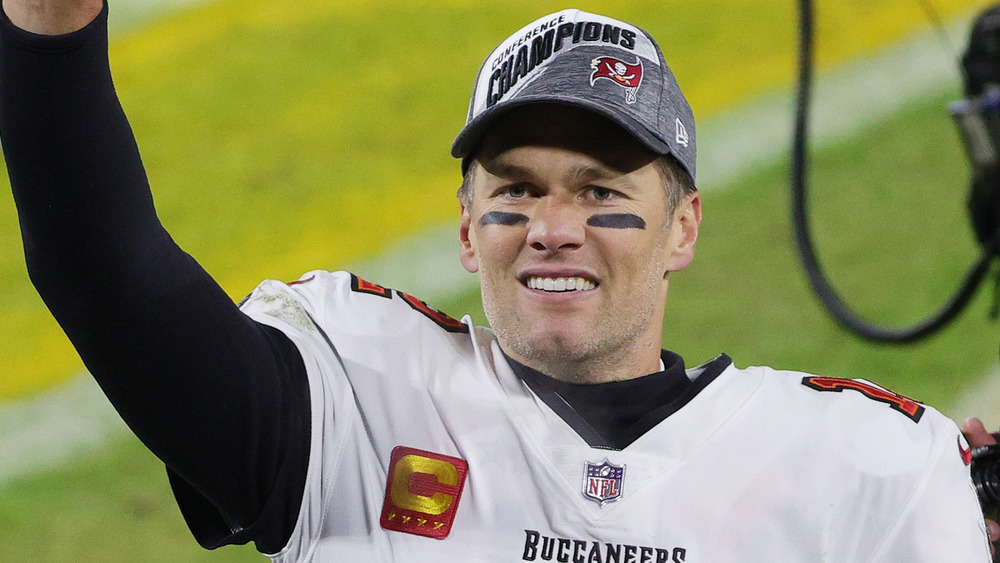 Tom Brady sonriendo con el brazo levantado sobre un campo de fútbol