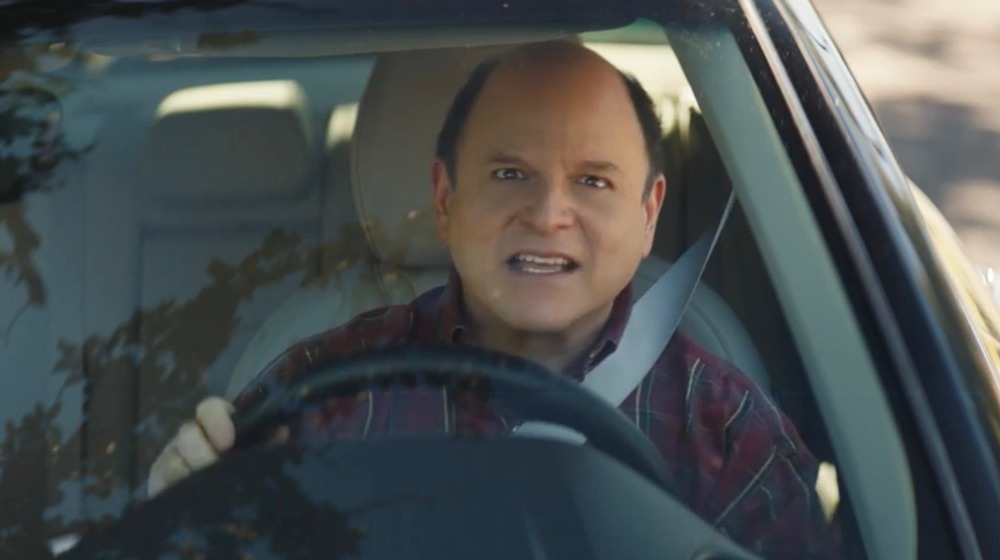 Jason Alexander mirando al frente desde el asiento del conductor de un automóvil