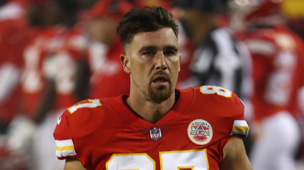 Travis Kelce, rostro serio, de uniforme, en el campo, pelo más largo, perilla