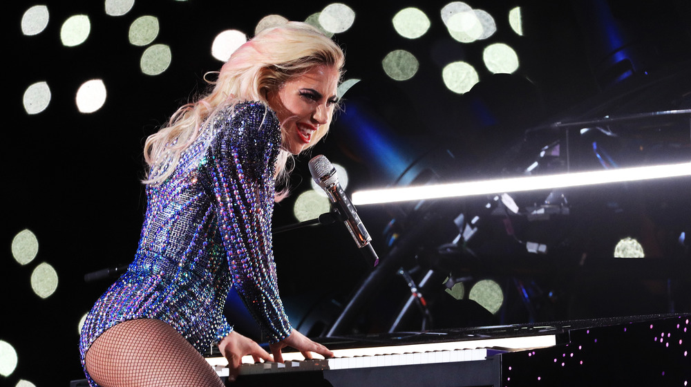 Lady Gaga levanta la pierna sobre su piano y canta en el micrófono en el espectáculo de medio tiempo del Super Bowl 2017