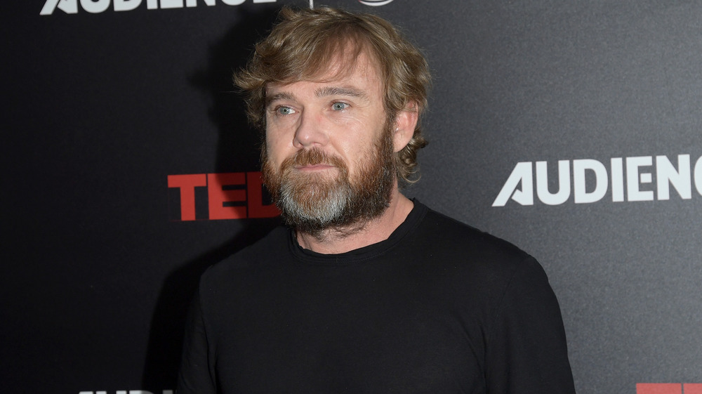 Ricky Schroder frente al muro promocional de TED