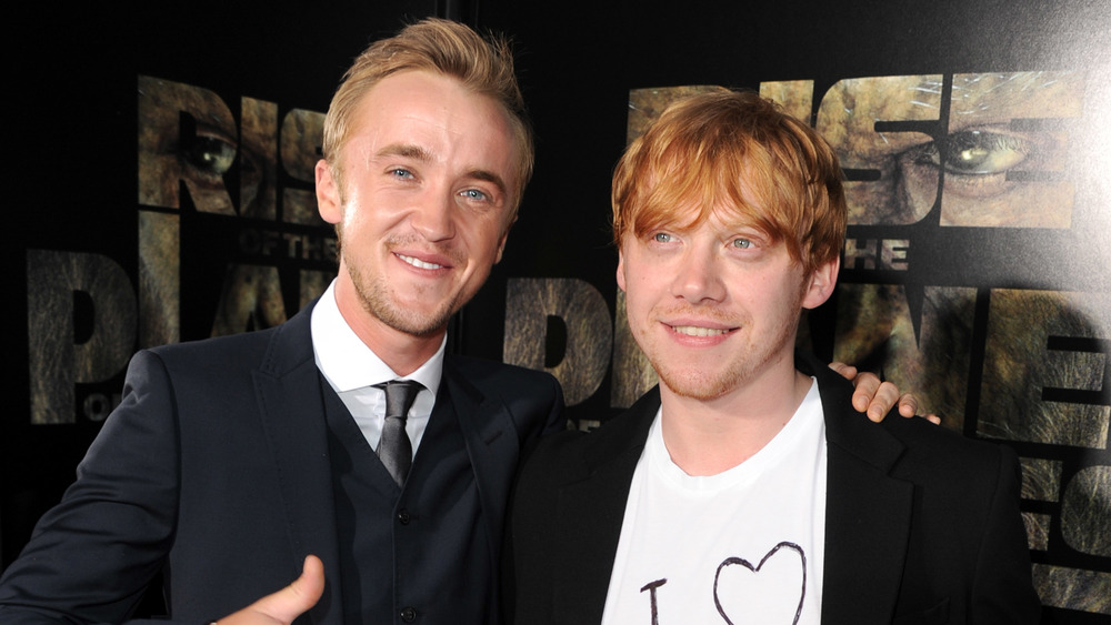 Tom Felton y Rupert Grint sonriendo mientras posan del brazo en el estreno de una película