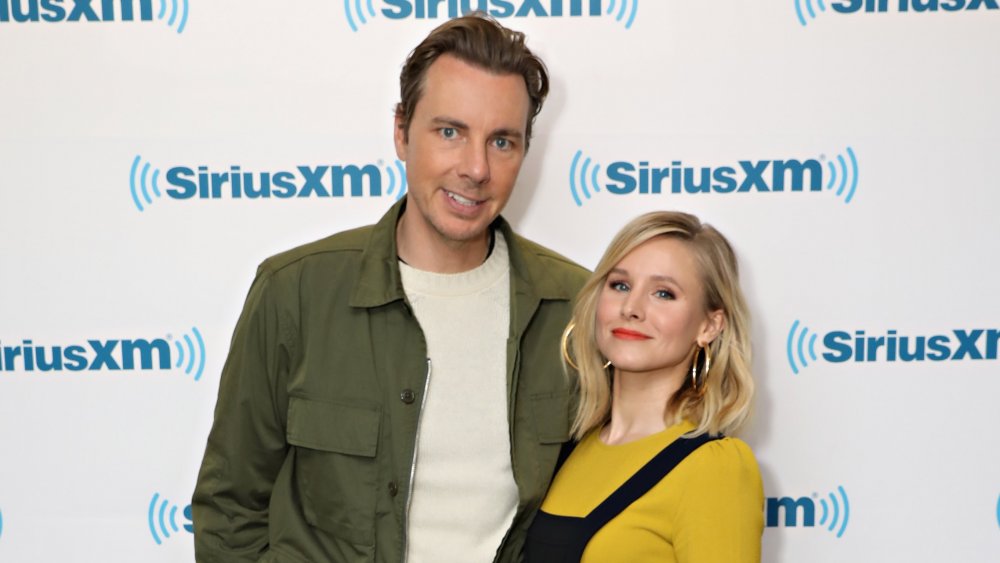 Dax Shepard y Kristen Bell frente al muro promocional de SiriusXM