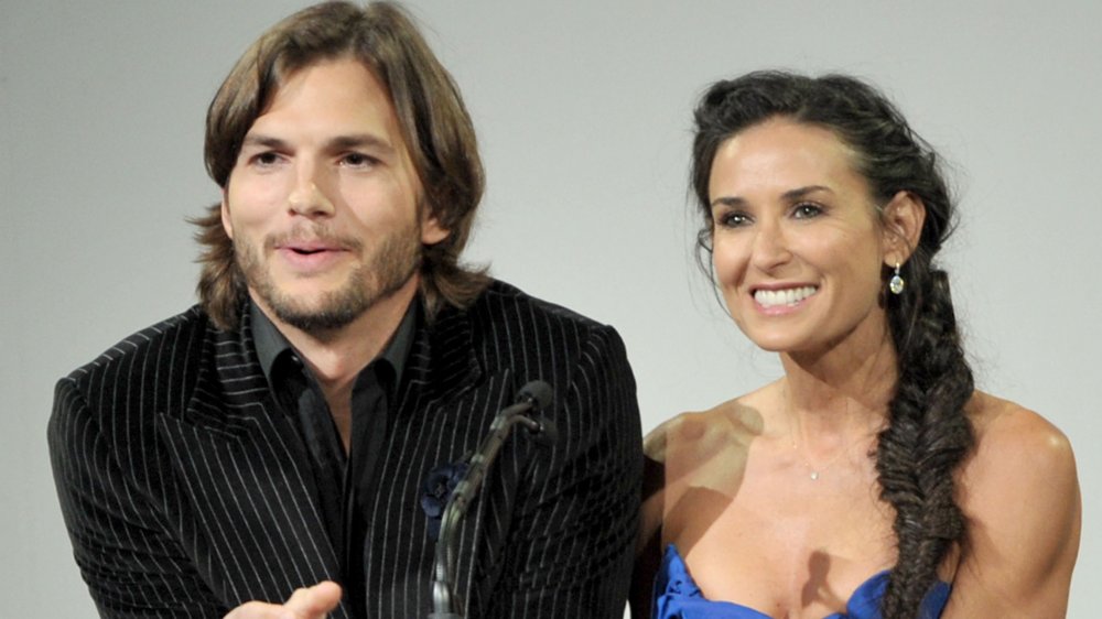 Ashton Kutcher y Demi Moore de pie uno al lado del otro detrás de un podio y sonriendo