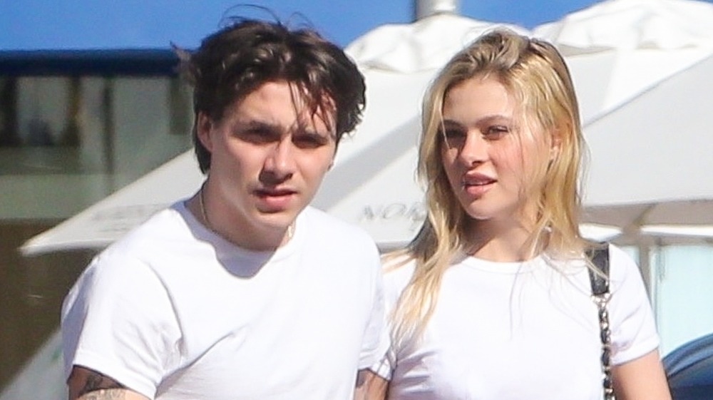 Brooklyn Beckham y Nicola Peltz vistiendo camisetas blancas a juego, caminando afuera 