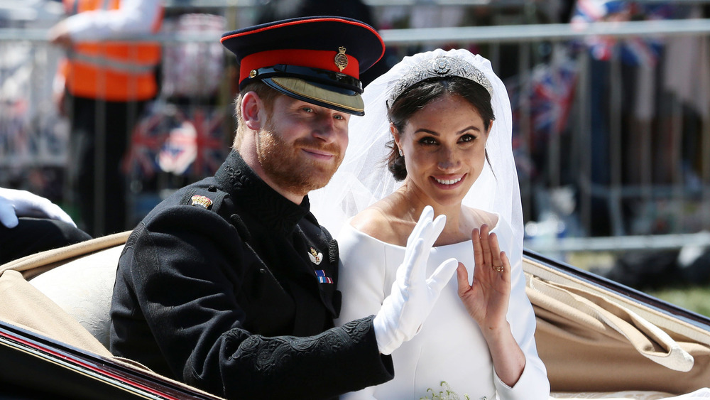 El príncipe Harry y Meghan Markle sonriendo y saludando a los fanáticos el día de su boda 