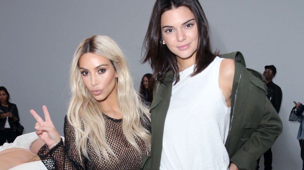 Kim Kardashian mostrando un letrero con Kendall Jenner en un desfile de modas