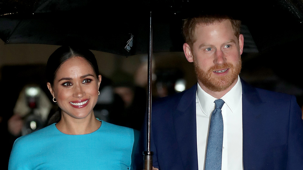 Meghan Markle y el príncipe Harry sonriendo bajo un paraguas