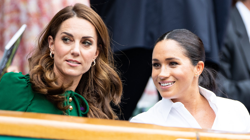 Kate Middleton y Meghan Markle se sientan y hablan juntas mirando a su derecha, mientras Markle sonríe