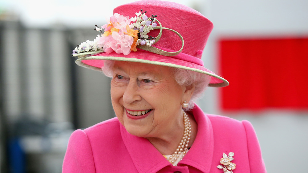 La reina Isabel II sonriendo en un evento vestida de rosa brillante