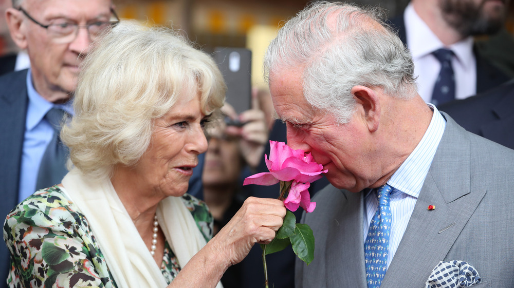 Camilla Duquesa de Cornualles sosteniendo una flor para que el príncipe Carlos la huela